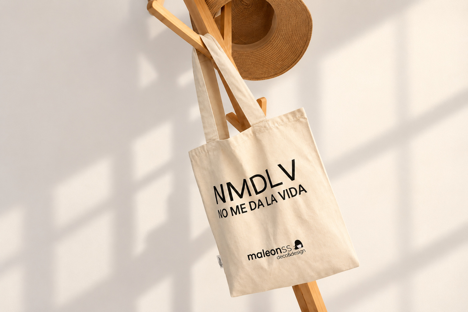 Bolsa NMDLV sobre un perchero de madera, con sombrero y una pared clara ampliada a los lados.