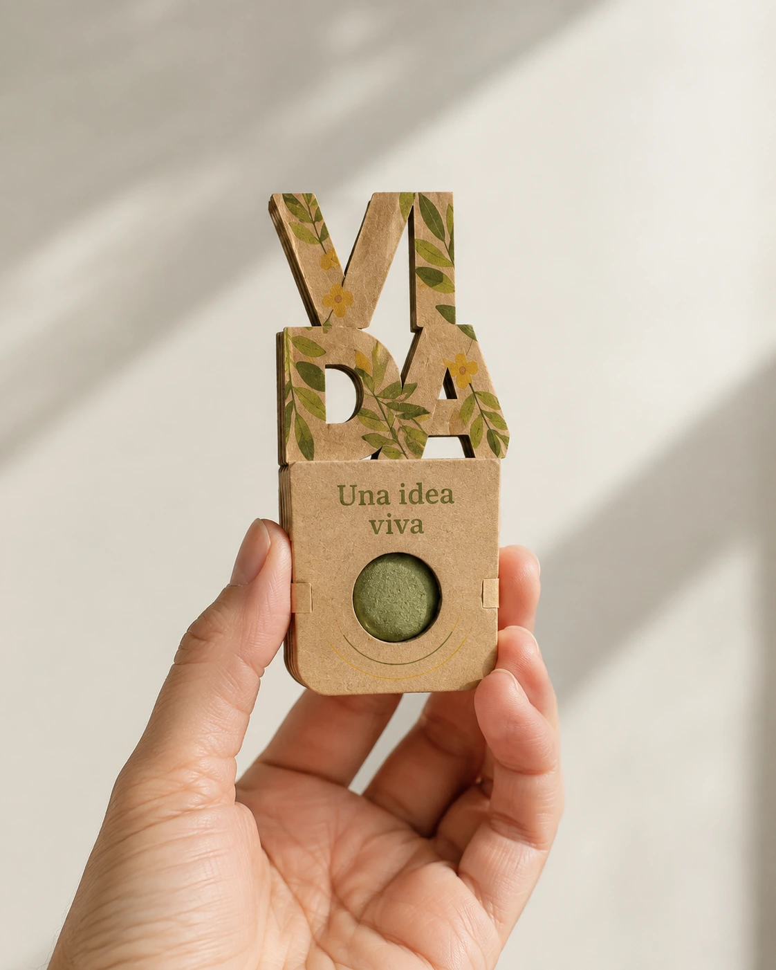 Bomba de semillas con solapa de cartón personalizable; propuesta de personalización en color con la frase «Una idea viva», sostenida en la mano.