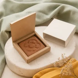 Figura cuadrada de semillas con relieve floral dentro de una caja de cartón abierta.