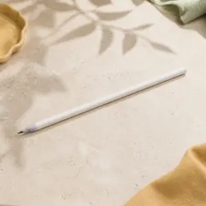 Lápiz blanco de papel reciclado con semillas sobre piedra clara, con la punta de grafito visible.