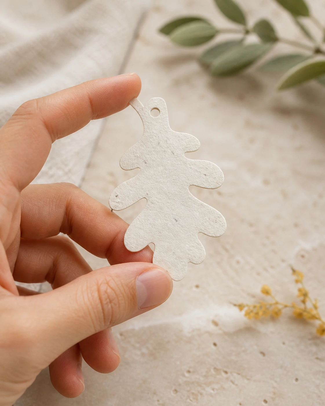 Mano mostrando una propuesta de figura de hoja en papel con semillas