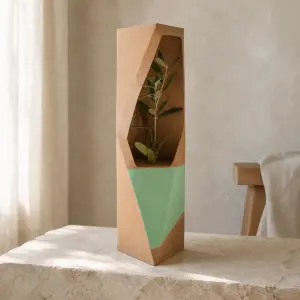 Árbol pequeño en caja escultórica de cartón con ventana abierta.