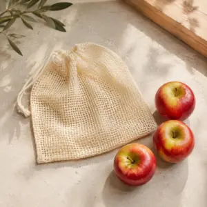 Bolsa de malla de algodón con tres manzanas como ejemplo de selección, presentación sobre superficie natural