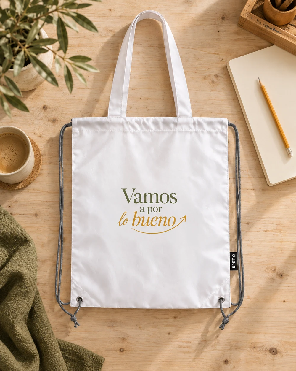 Bolsa Impulso blanca con diseño a color sobre una mesa de madera clara, junto a una libreta y una taza.
