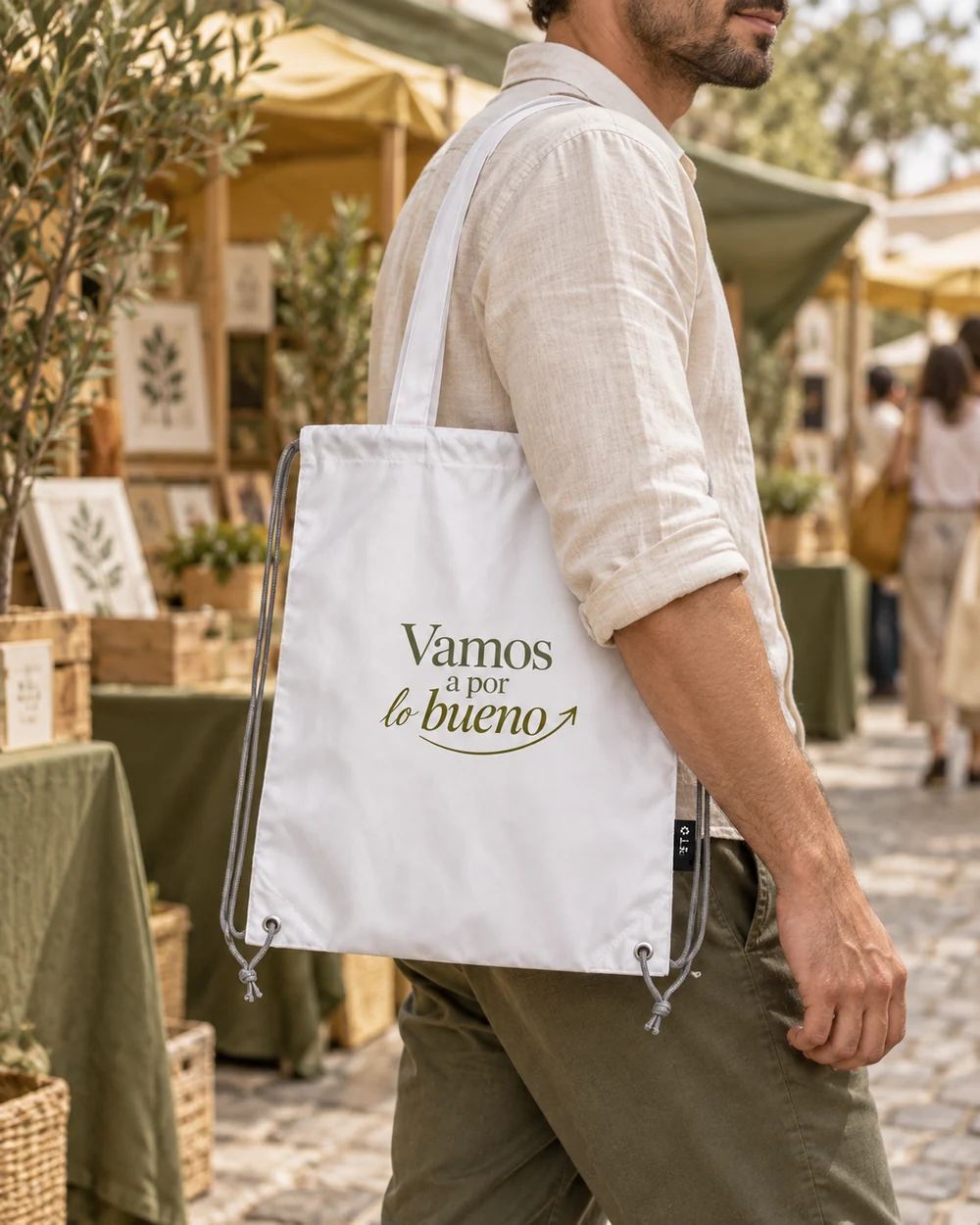 Bolsa Impulso blanca llevada al hombro, con el diseño «Vamos a por lo bueno» a una tinta oliva.